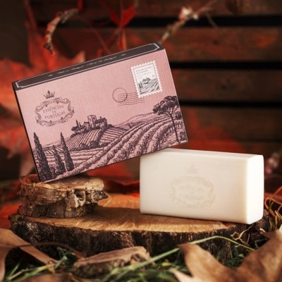 Sabonete branco com embalagem rosa desenhada com selo postal sobre madeira e folhas secas