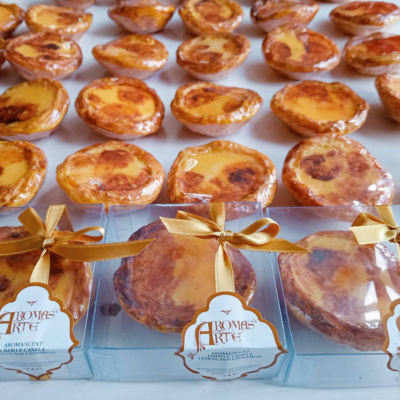 Pastéis de nata embalados e expostos em caixas transparentes com fita dourada e etiquetas da marca Aromas Arte