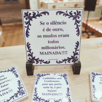 Placa decorativa branca com texto em português e bordas roxas sobre mesa de madeira clara.