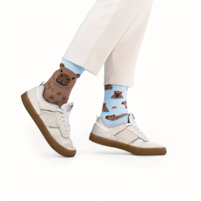 Meias divertidas com padrão de lontras em fundo azul claro e castanho, usadas com calças brancas e sapatilhas brancas.