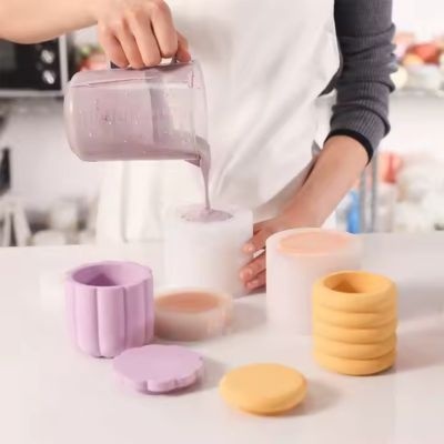 Pessoa a verter líquido roxo em copo branco com copos e tampas de silicone lilás e amarelos na mesa