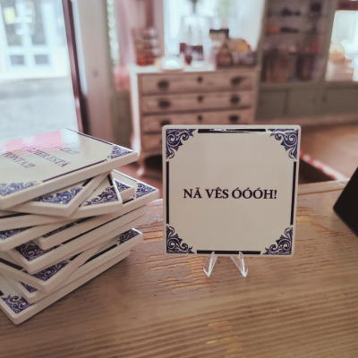 Azulejos de cerâmica com texto em português num suporte sobre mesa de madeira