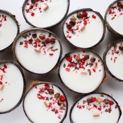 Velas brancas em cascas de coco com decoração colorida sobre fundo branco