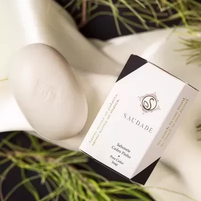 Sabonete branco oval com embalagem branca e preta com texto SAUDADE ao lado