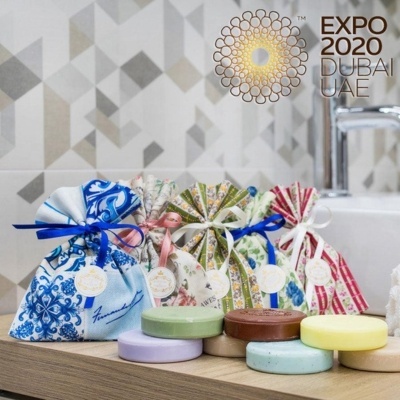 Saquinhos de tecido e sabonetes coloridos em bancada de madeira com parede geométrica e torneira ao fundo