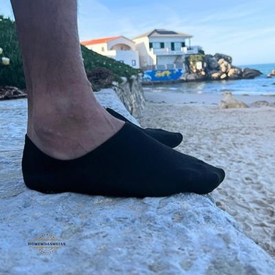 Meias pretas tipo sapatilha sobre pedra junto à praia