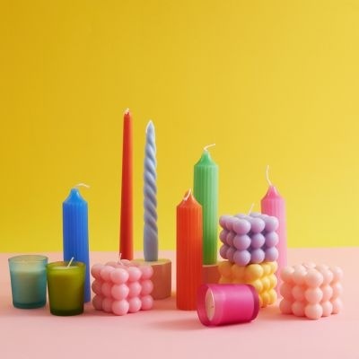 Velas decorativas coloridas variadas sobre superfície rosa e fundo amarelo
