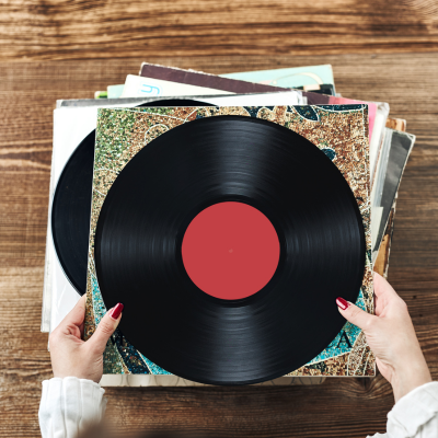 Disco de vinil preto com etiqueta vermelha e capas coloridas numa mesa de madeira.