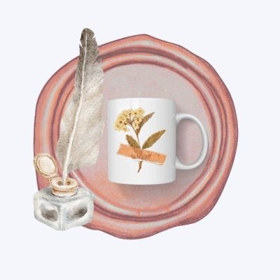 Caneca branca com flor amarela sobre prato rosa com tinteiro e pena
