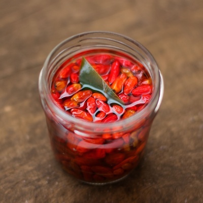 Frasco de vidro com malaguetas vermelhas em óleo e uma folha verde no topo