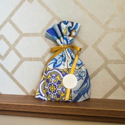 Saco decorativo de tecido colorido com fita dourada numa prateleira de madeira