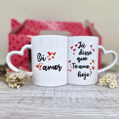 Par de canecas brancas com pega em forma de coração e texto romântico em português