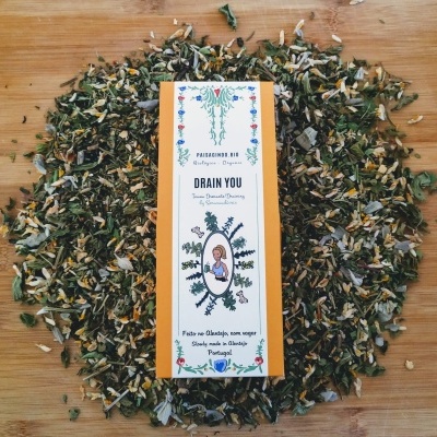Pacote de chá Drain You rodeado por folhas de chá soltas em mesa de madeira