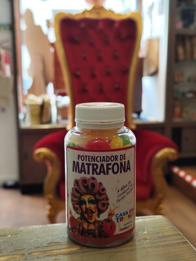 Frasco de pastilhas coloridas rotulado POTENCIADOR DE MATRÁFONA em frente a cadeira vermelha