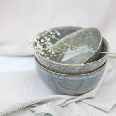 Duas tigelas cinzentas empilhadas com ramo de flores brancas delicadas sobre um pano cinzento.