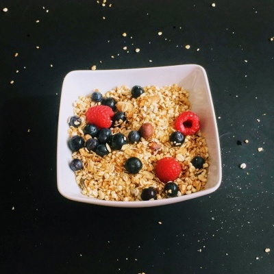 Tigela quadrada branca com granola e frutos silvestres em fundo preto