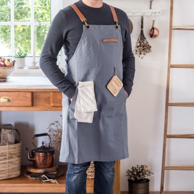 Homem com avental cinzento com alças castanho claro em cozinha rústica