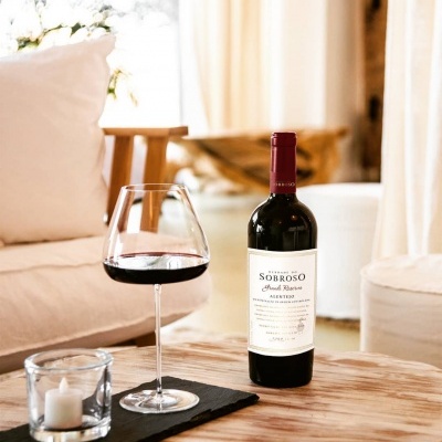 Garrafa de vinho tinto SOBROSO com taça e vela numa mesa de madeira ao lado de sofá branco