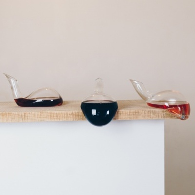 Três decantadores de vinho de vidro com diferentes tipos de vinho, sobre prateleira clara