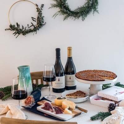 Mesa posta com vinho, queijos, carne e bolo decorada em ambiente acolhedor com guirlandas e elementos naturais