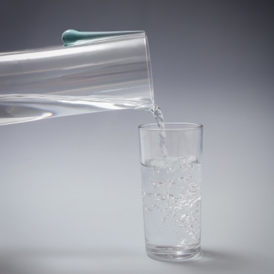 Copo de vidro a ser preenchido com água de um jarro transparente.