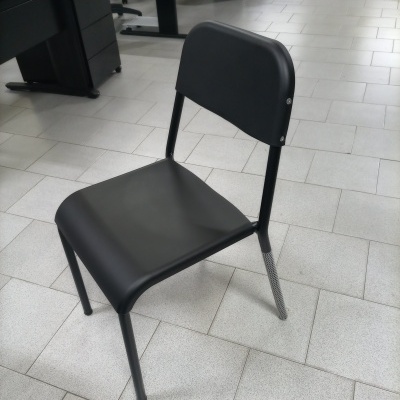 Cadeira preta de metal com encosto arredondado sobre chão de azulejos cinza em escritório