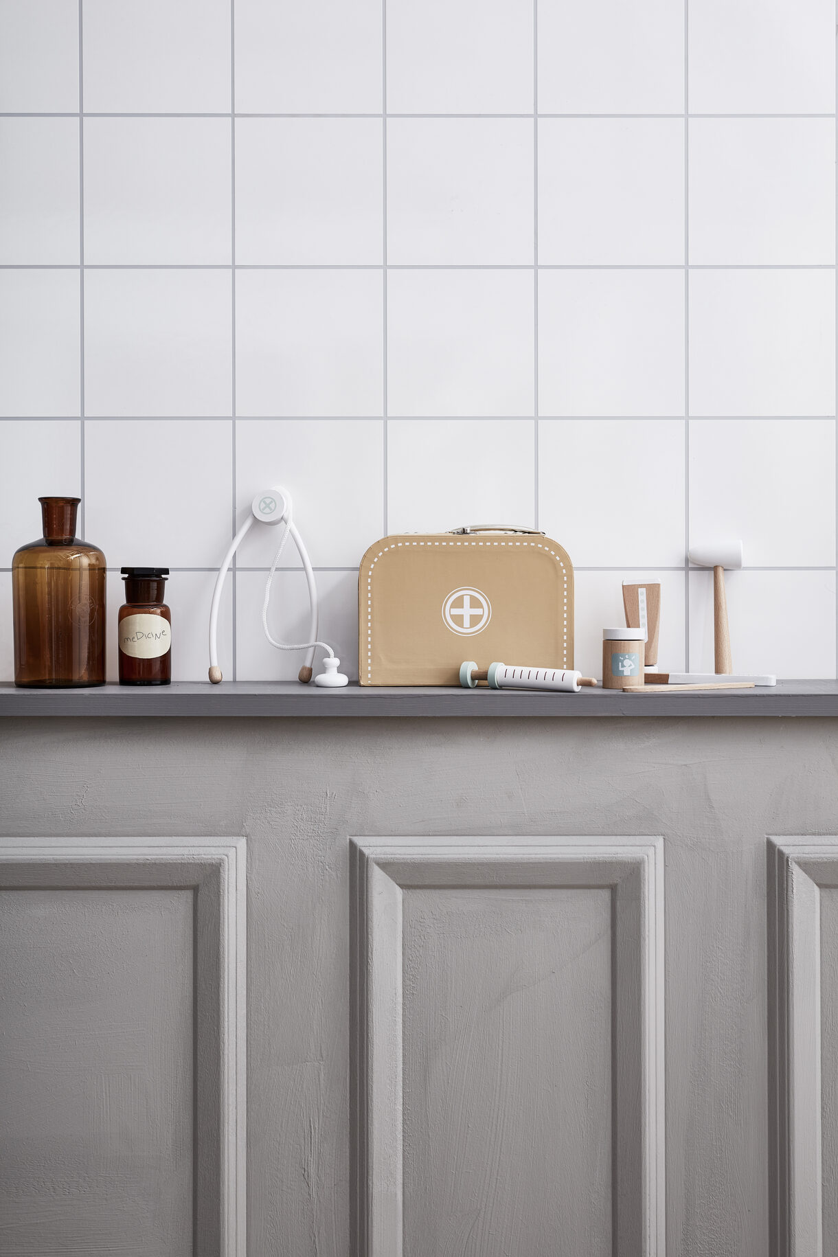 KIT MÉDICO Produtos médicos organizados numa prateleira cinzenta com azulejos brancos ao fundo