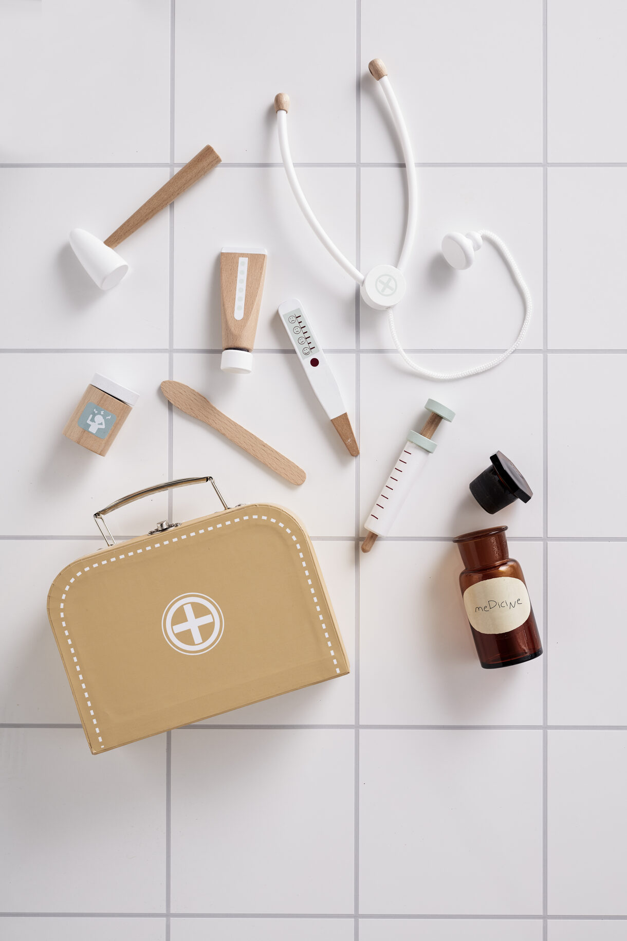 KIT MÉDICO Brinquedo kit médico com mala bege e acessórios brancos e castanhos em azulejos brancos