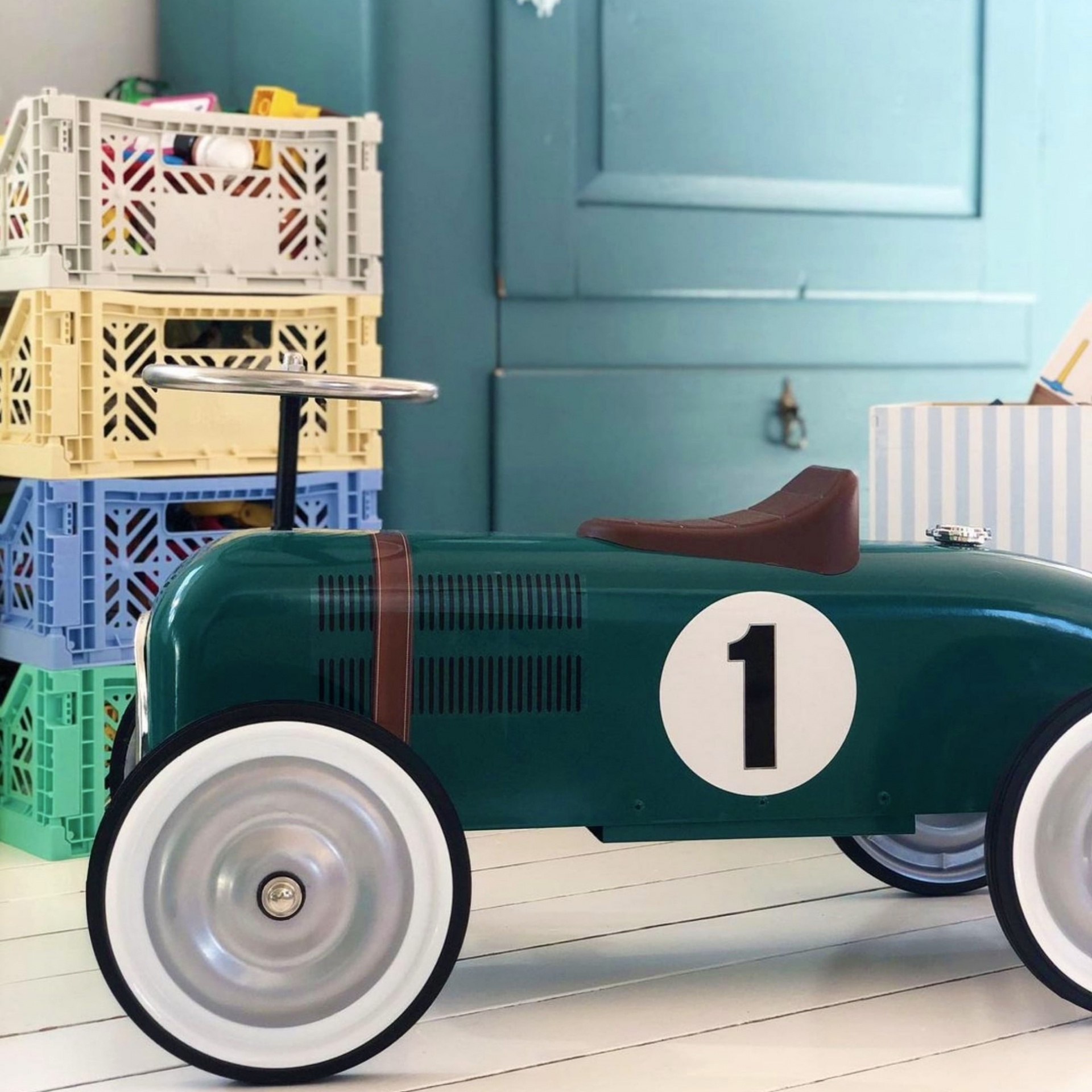 CAIXA EMPILHÁVEL | MAXI Triciclo infantil verde com roda branca e número 1 junto a caixas de plástico coloridas