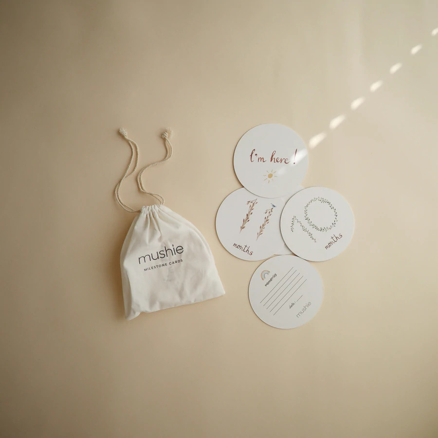 CARTÕES MILESTONE Sacos de tecido branco com cartões redondos e textos variados numa superfície bege