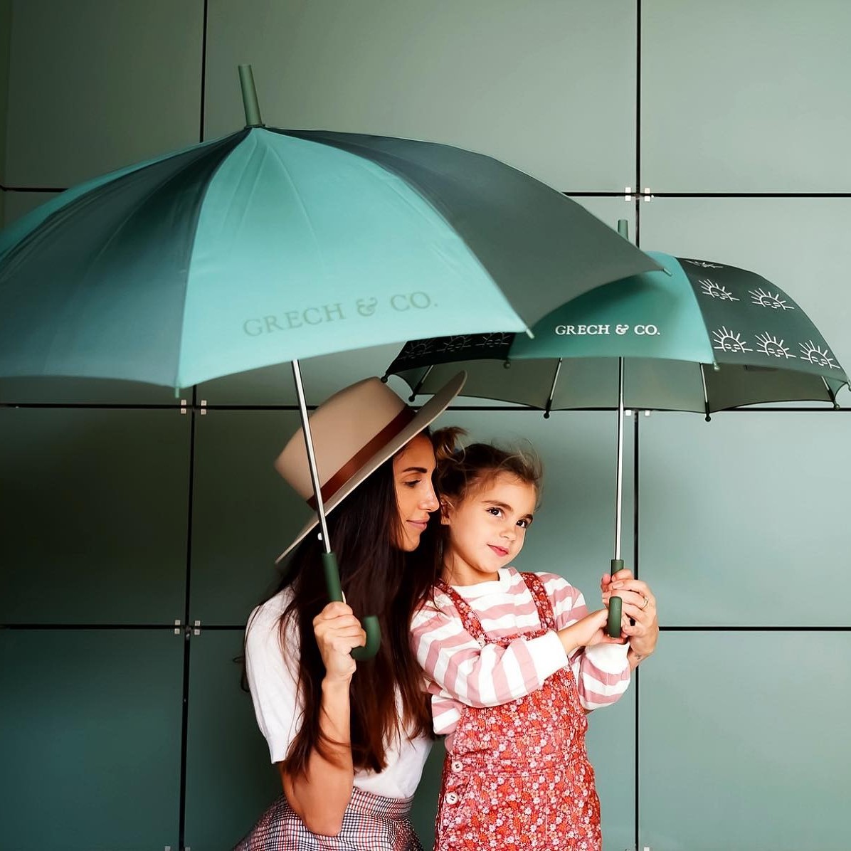 CHAPÉU DE CHUVA SUSTENTÁVEL | MOMMY & ME Duas pessoas segurando guarda-chuvas com texto GRECH & CO.