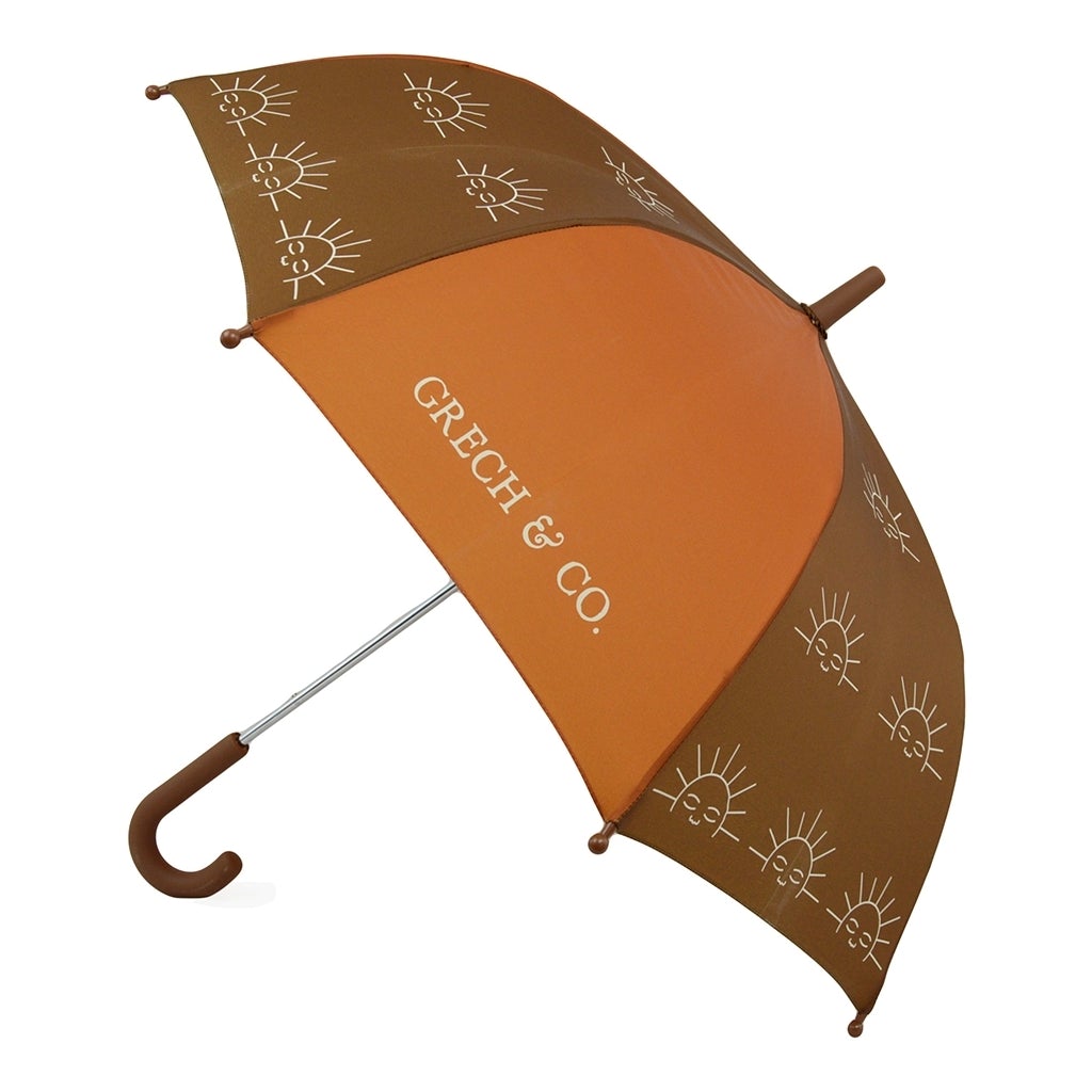 CHAPÉU DE CHUVA SUSTENTÁVEL | MOMMY & ME Guarda-chuva castanho e laranja com padrão de desenhos de sol e texto GRECH & CO.