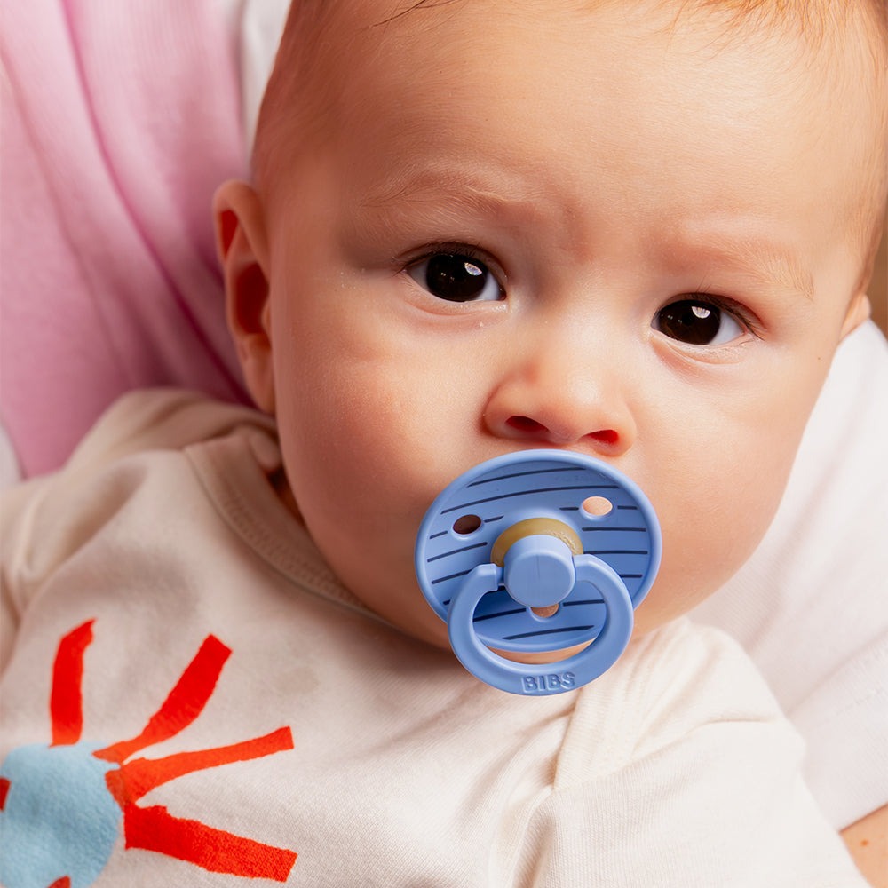 BIBS COLOUR | STUDIO EDITION Bebé com chupeta azul e camisola branca com estampa vermelha e azul