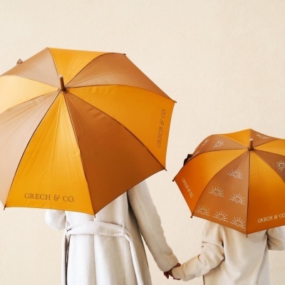 Dois guarda-chuvas amarelo e castanho com texto GRECH & CO., segurados por pessoas com casacos claros
