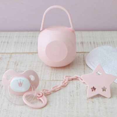 Chupeta rosa, cadeia plástica e estojo rosa sobre madeira clara