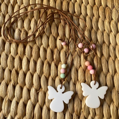 Dois colares com pingentes de anjo brancos e contas coloridas em cordões castanhos sobre fundo trançado