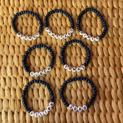 Pulseiras com contas azuis e letras com nomes em contas brancas sobre superfície bege texturizada