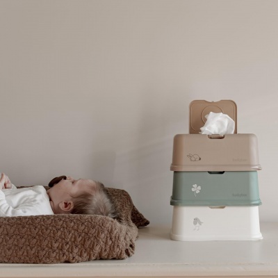 Três caixas dispensadoras de tecidos empilhadas junto a um bebé deitado numa almofada castanha