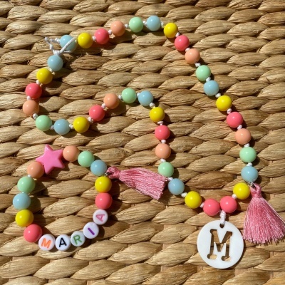 Colar e pulseira de contas coloridas com letras e pingentes sobre fundo trançado
