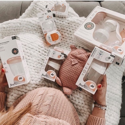 Produtos para bebé Nio First Moments com biberões e extrator sobre manta tricotada branca