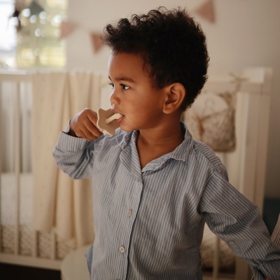 Criança com camisa azul claro às riscas segurando mordedor branco em quarto com berço