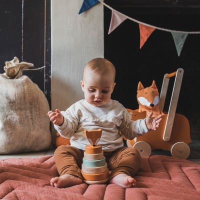 Bebé a brincar com brinquedo de madeira sentado num tapete cor terra, carrinho e peluche de raposa ao fundo