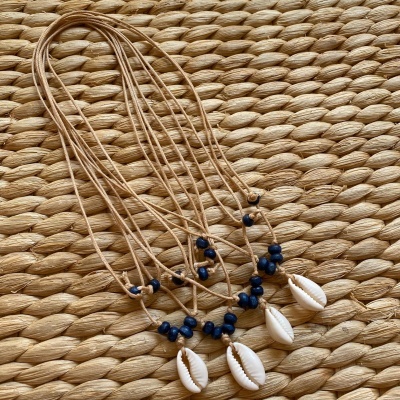 Colar de cordão bege com concha branca e contas azuis sobre superfície de fibra trançada