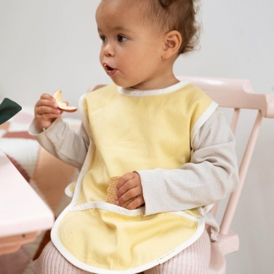 Criança com babete amarelo e roupa cinza numa cadeira rosa com bolacha e maçã