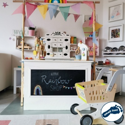 Quiosque de madeira branca com quadro-negro e carrinho de compras de brinquedo amarelo e cinza