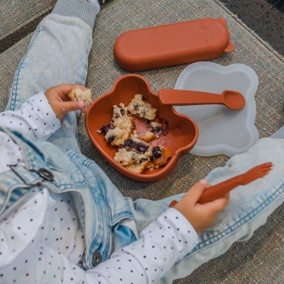 Prato em forma de urso castanho com colher e tampa, e mão segurando pedaço de bolo