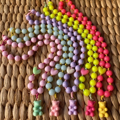 Colares coloridos com contas e pingentes de ursinhos e corações sobre superfície de palha