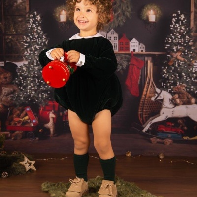 Criança com macaquito preto e gola branca segurando brinquedo vermelho em cenário natalício