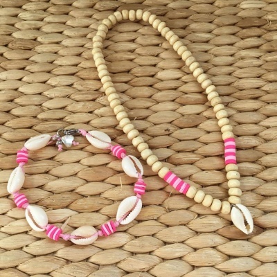 Conjunto de colar e pulseira com contas de madeira, conchas e contas cor-de-rosa sobre superfície trançada bege