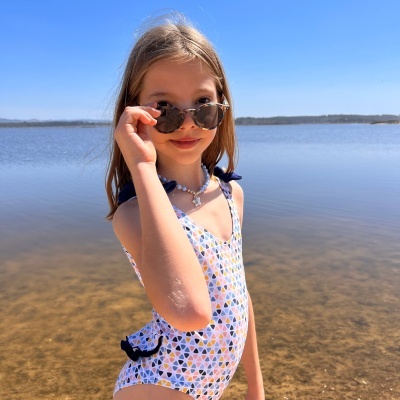 Menina de fato de banho colorido com óculos de sol numa praia